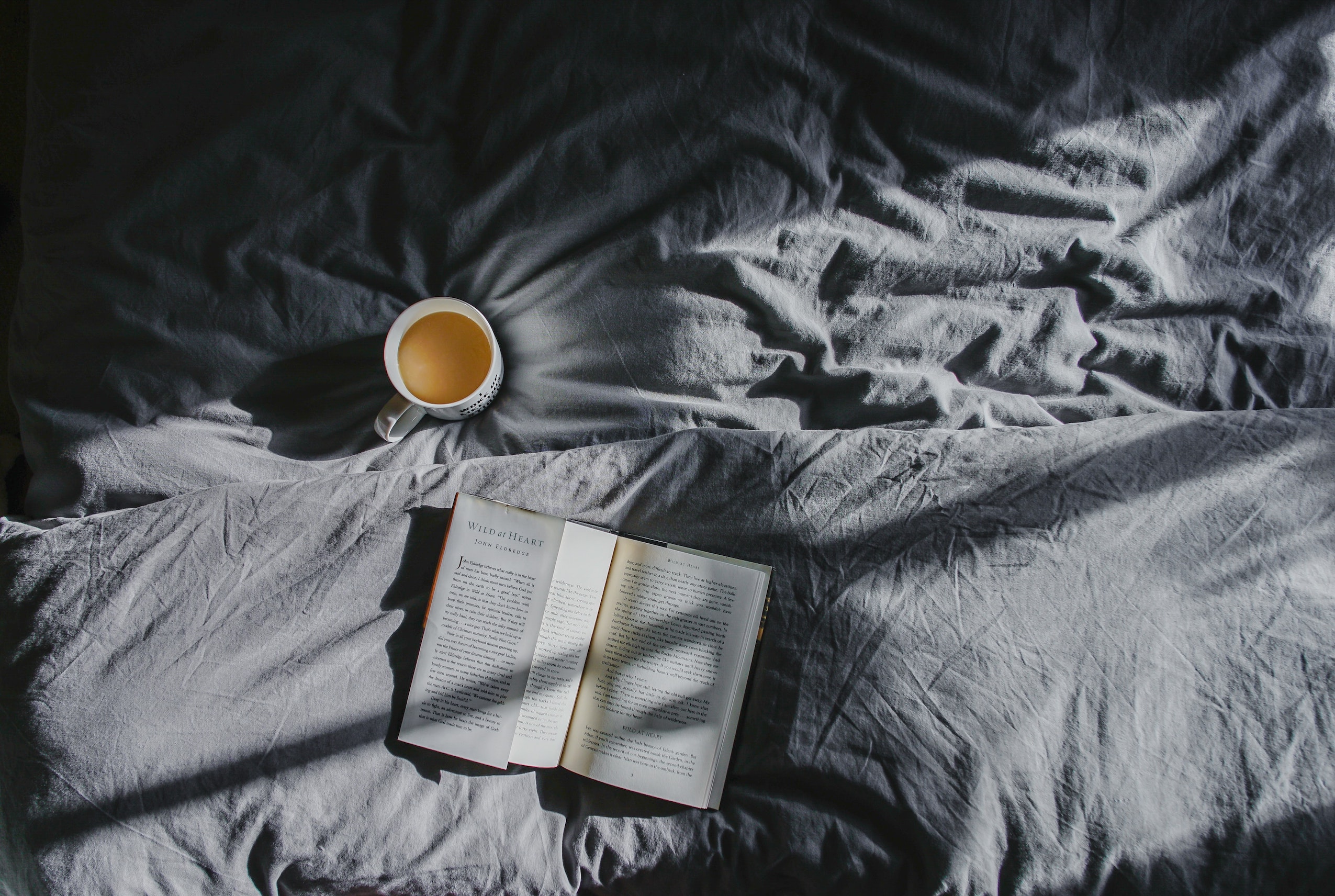 open book and mug on grey bed sheets