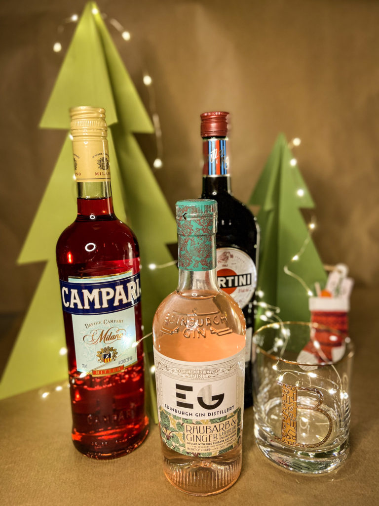 bottle of campari, gin liqueur, martini and a rocks glass in front of a festive background