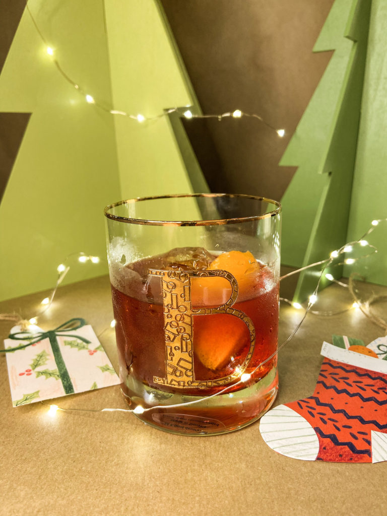 rhubarb and ginger negroni in a rocks glass garnished with a slice of orange in front of a festive background