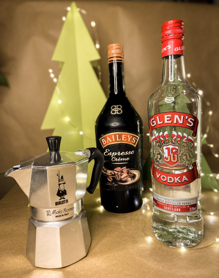 bottle of baileys, bottle of vodka, and coffee pot in front of a festive background